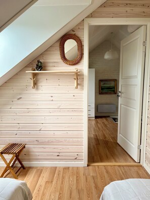 Une pièce avec un plafond en pente, des murs en bois, une petite étagère ornée d’un objet décoratif, un miroir en osier et un banc en bois.
