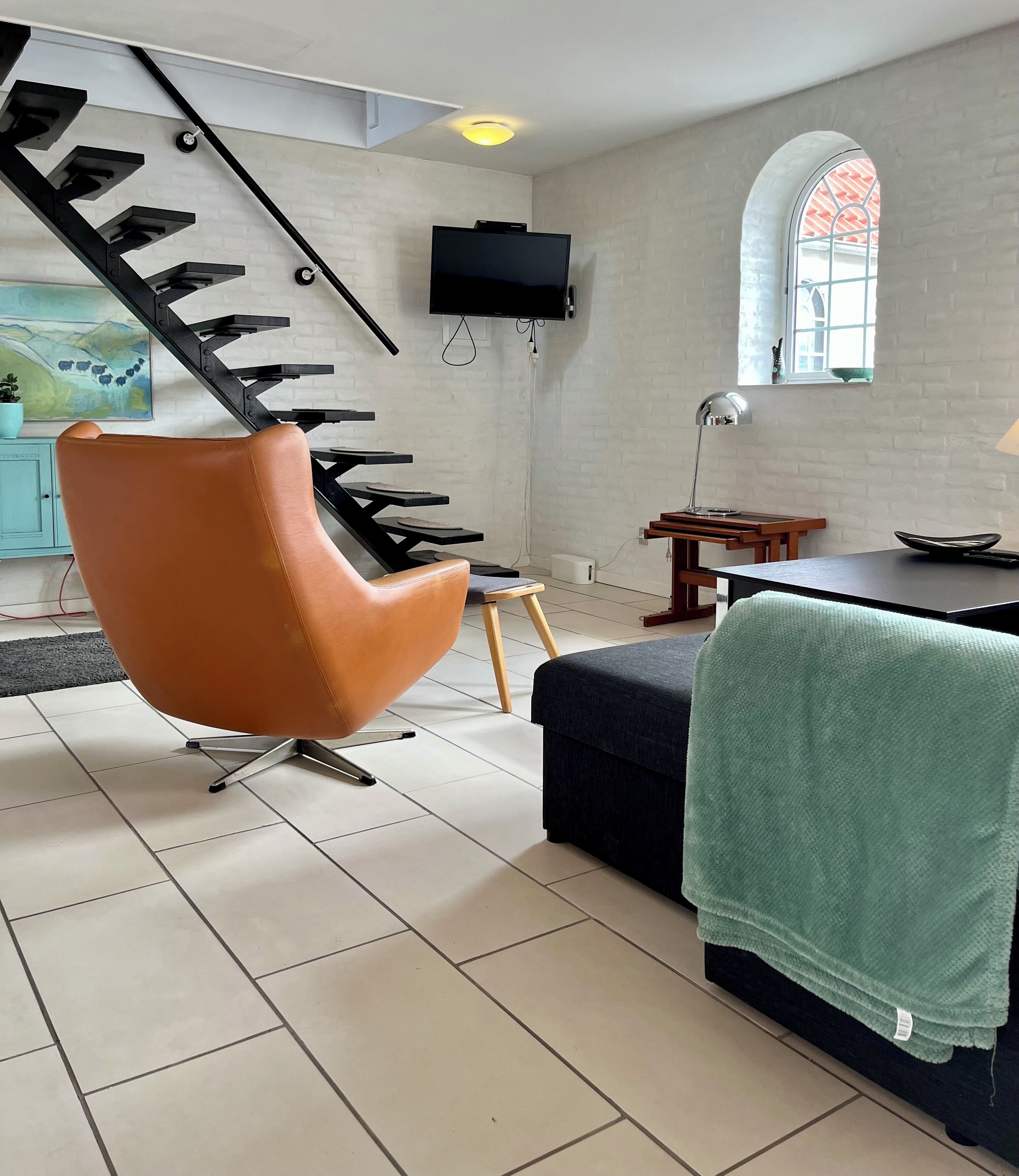 A modern living room with a unique black staircase, a flat-screen TV mounted on the wall, and a cozy seating area with a green throw blanket.