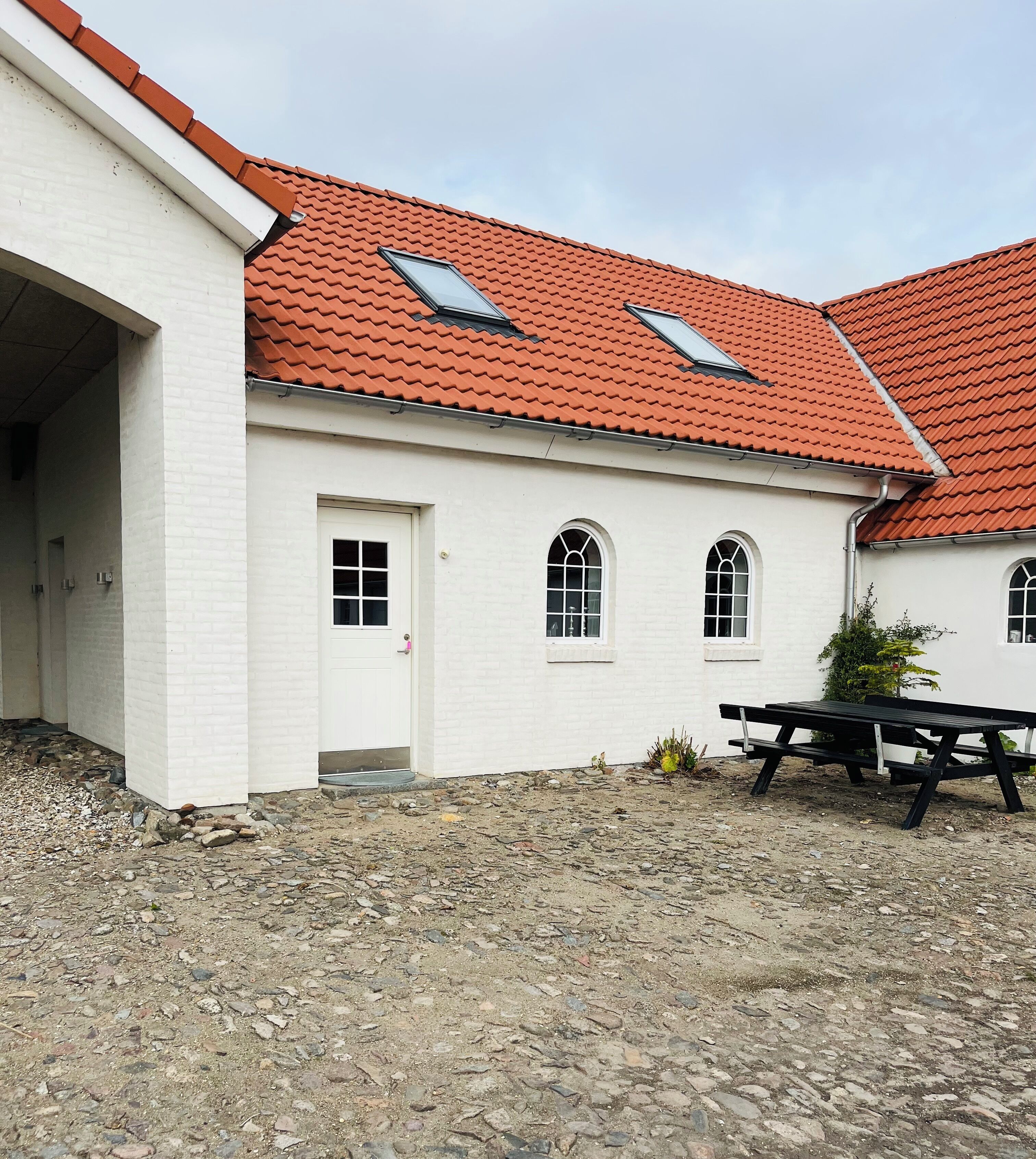 Ein Gebäude mit rotem Ziegeldach, weißen Wänden und einer Tür mit einer kleinen Veranda.
