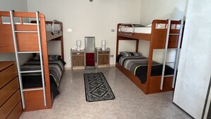 A room with two bunk beds, a small desk with a chair, a red sofa, a chandelier, and a tiled floor.