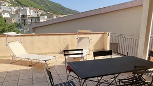 An outdoor terrace with a table and chairs, a view of a hillside town, and a covered area with a ceiling.