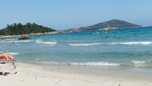 A beach with clear blue water, people swimming, and a chair on the sand.
