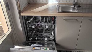 A compact kitchen with a built-in dishwasher, a sink, and a backsplash with a floral pattern.