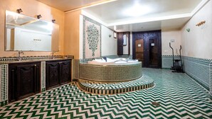 A bathroom with a central circular bathtub, a large mirror above the sink, and patterned tile flooring.