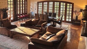 A spacious living room with a high ceiling, large windows, and a fireplace.