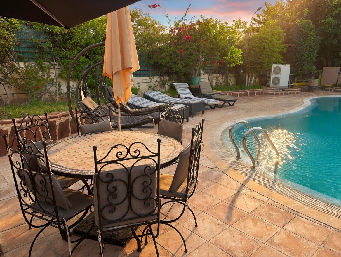 A poolside area with a round table and chairs, lounge chairs, and a covered seating area.