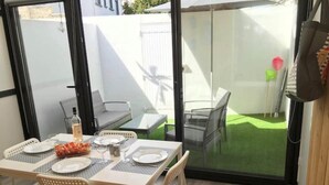 Un coin repas avec une table dressée pour quatre personnes, une bouteille de vin et un panier de fruits.