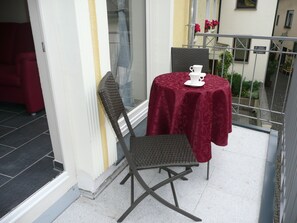 Ein Balkon mit Tisch und Stuhl, ein roter Sessel und Blick auf die Straße.