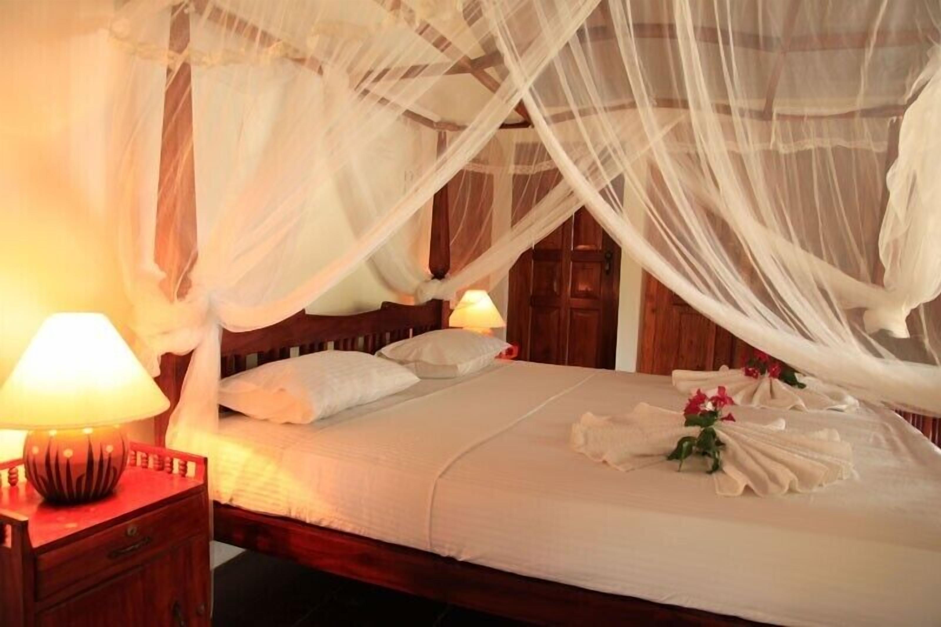 A bed with a canopy, bedside lamps, and a neatly made bed with towels and flowers.