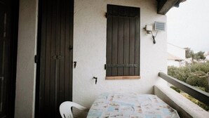 A balcony with a table and chairs, a closed door, and a window with shutters.