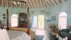 Un dormitorio amplio con una cama grande, un ventilador de techo y vistas al exterior por una puerta.