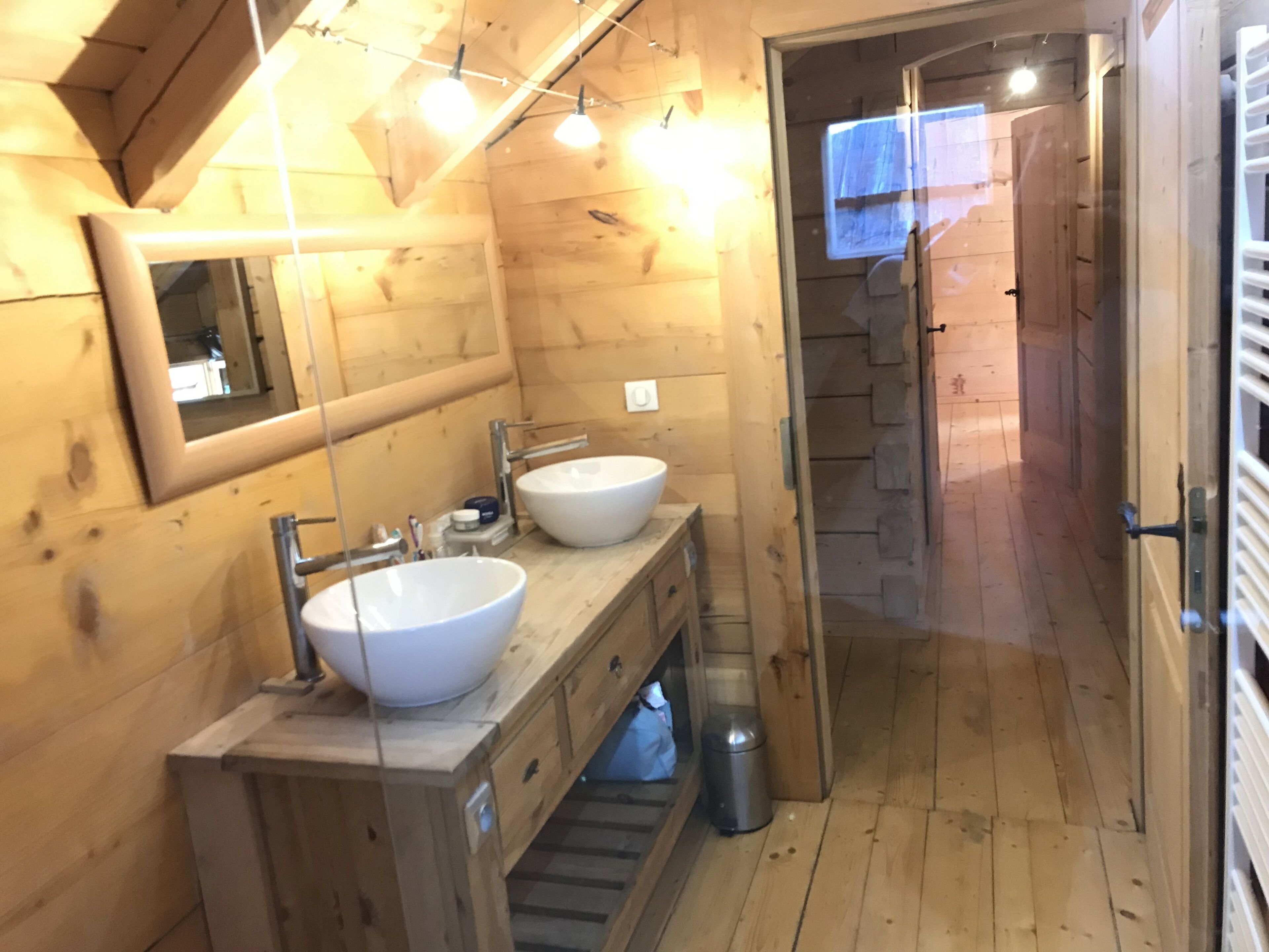 Een houten badkamer met twee wastafels, een spiegel en een douchehoek.