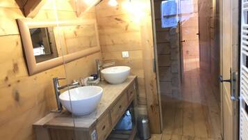 Een houten badkamer met twee wastafels, een spiegel en een douchehoek.