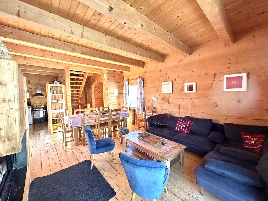 Een houten blokhut van binnen met een eethoek, een bank en een open haard.