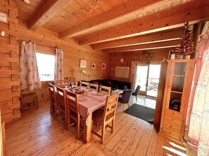 Interior de uma cabana de madeira com uma mesa de jantar, cadeiras, um sofá e um armário.