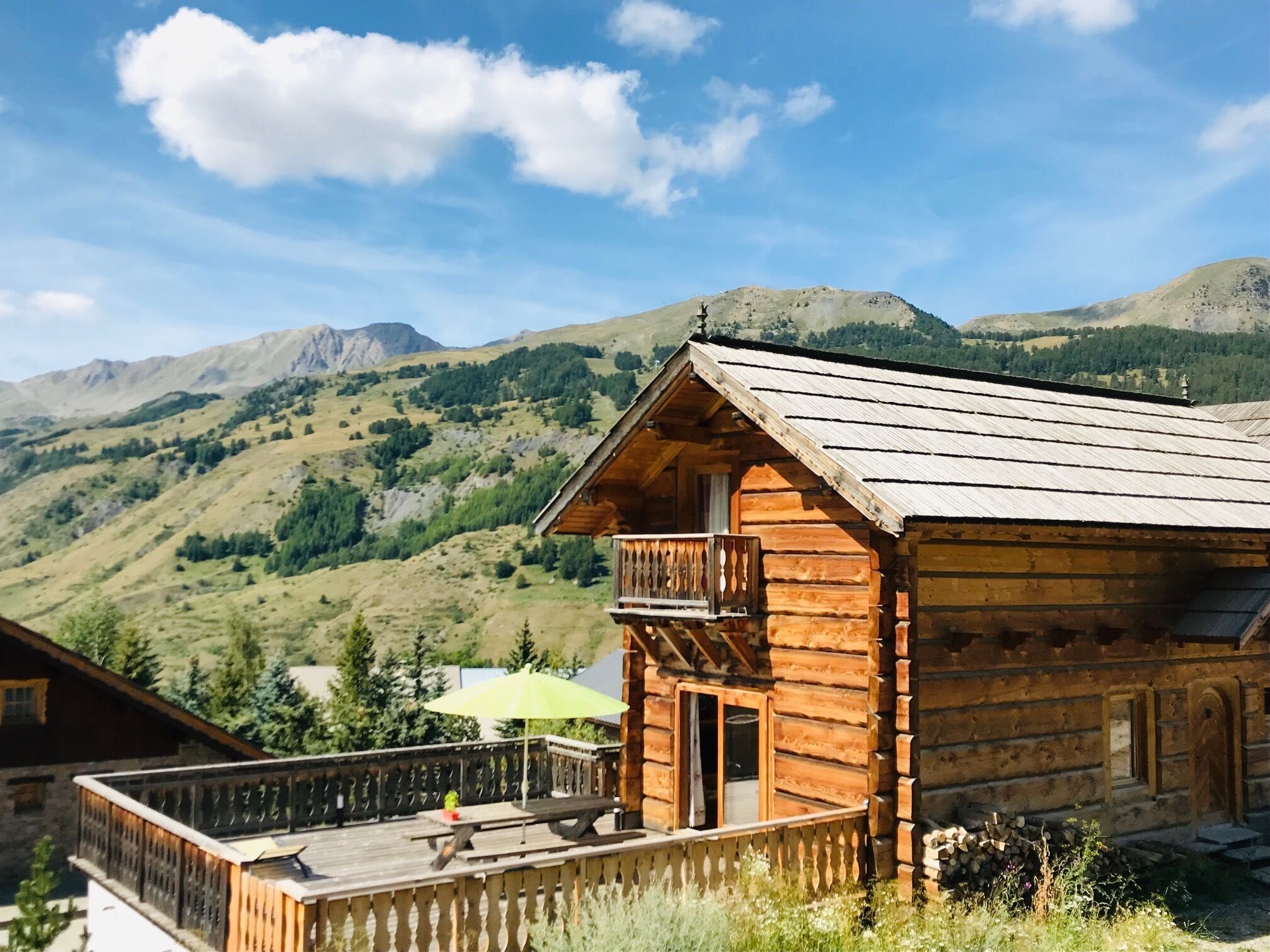 Een houten chalet met balkon, omringd door bergen en groen.