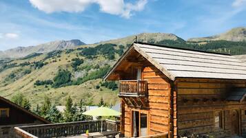 Een houten chalet met balkon, omringd door bergen en groen.