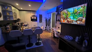 Uma sala de estar moderna com televisão, área de estar, cozinha e uma janela grande com vista para o verde.