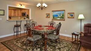 A dining area with a round table, ornate chairs, a chandelier, and a kitchen in the background.