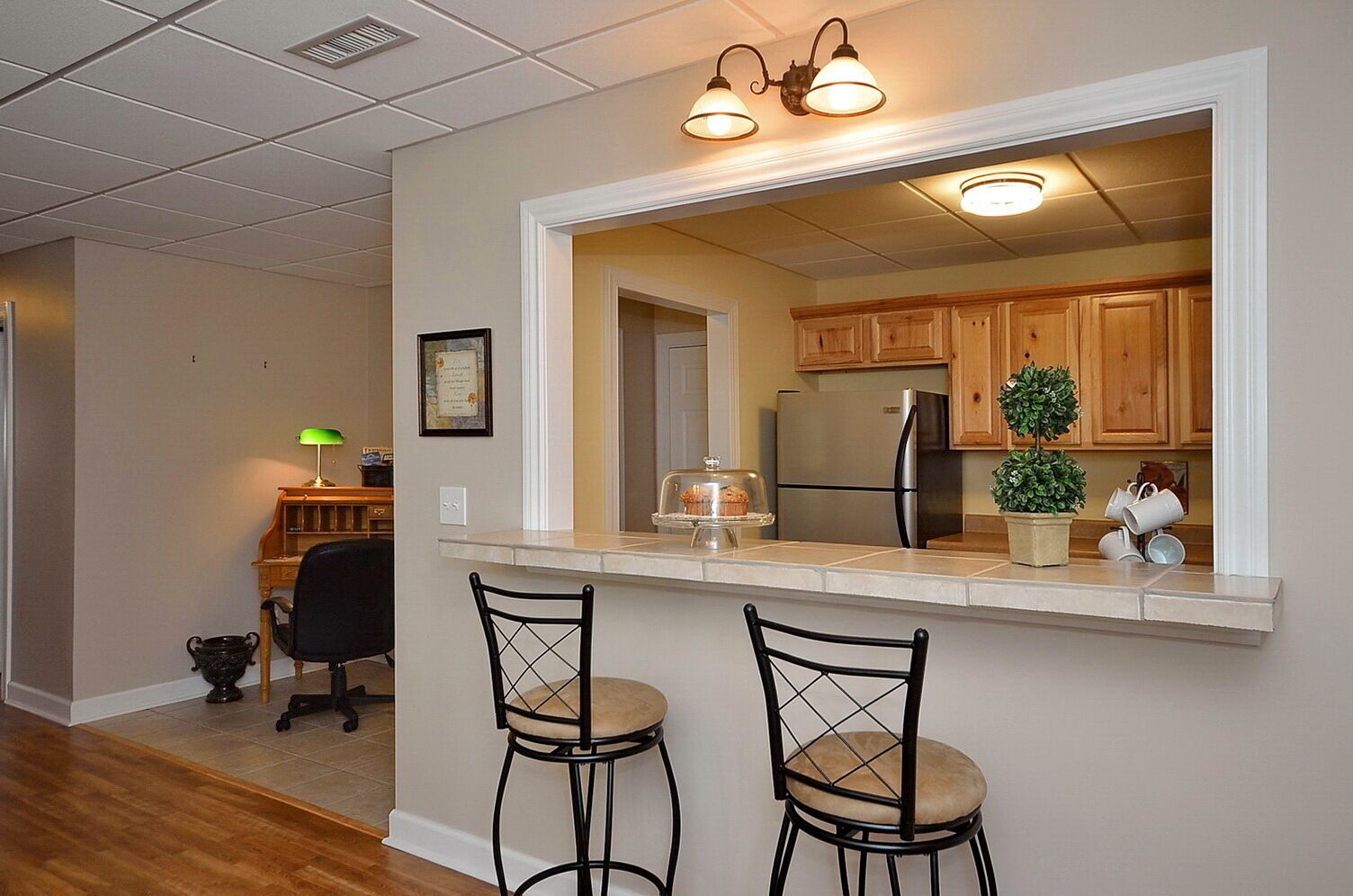 A kitchen with wooden cabinets, a stainless steel refrigerator, and a countertop with two bar stools.