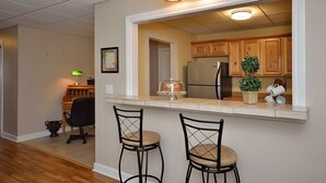 A kitchen with wooden cabinets, a stainless steel refrigerator, and a countertop with two bar stools.