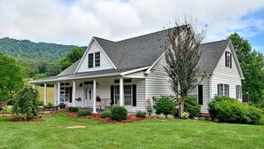 A two-story house with a covered porch, surrounded by a well-maintained lawn and various shrubs.