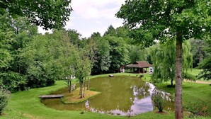 A serene pond surrounded by lush greenery, a gazebo, and a small building, likely a lodge or restaurant.