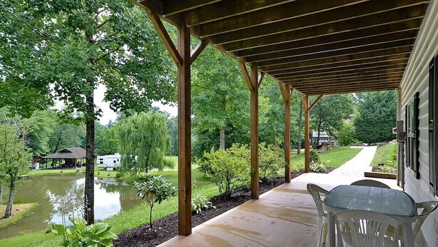 A covered patio with a view of a pond and a house in the background.