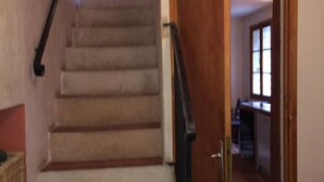 Eine Treppe mit Teppichstufen und Holhandläufen, die zu einem Raum führt, in dessen Nähe eine Küche durch eine offene Tür erkennbar ist.