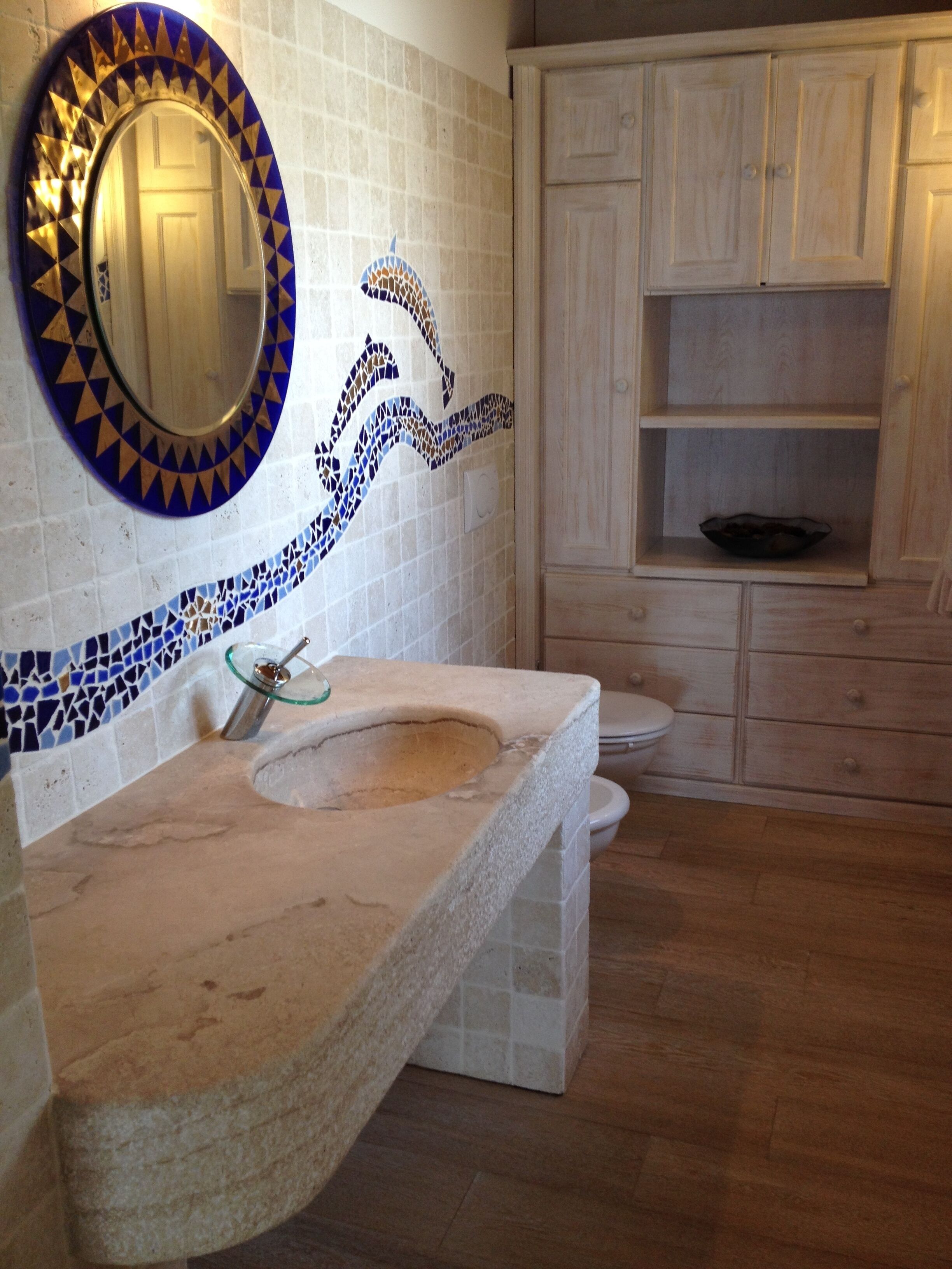 A bathroom with a mosaic backsplash, a sink, a toilet, and wooden cabinets.