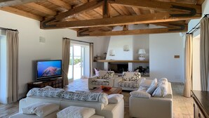 A spacious living room with a high wooden ceiling, a fireplace, and a television.