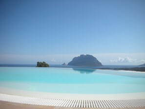 A clear blue pool with a view of a distant island and a clear sky.