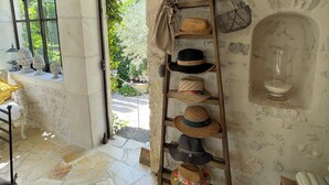 A rustic room with stone flooring, a wooden ladder with hats, a stone wall, and a window with a view of greenery. - Charming house in hamlet 18 th in the heart of the Luberon with swimming pool and air conditioning (Gordes)