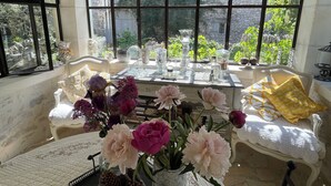 A sunlit room with a table set for dining, a chandelier, and a view of greenery outside. - Charming house in hamlet 18 th in the heart of the Luberon with swimming pool and air conditioning (Gordes)