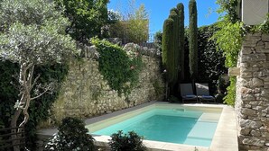 A swimming pool surrounded by stone walls and greenery, with a stone building and a bench in the foreground. - Charming house in hamlet 18 th in the heart of the Luberon with swimming pool and air conditioning (Gordes)