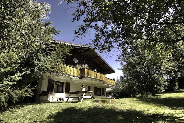 Face du chalet avec jardin, table, chaises longues et barbecue