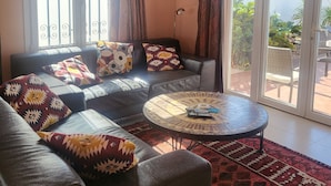 Uma sala de estar com sofá, mesa de centro e vista através de grandes portas de vidro.