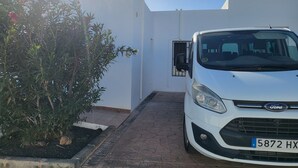 Um carro Ford branco estacionado em uma entrada de garagem, com um edifício branco ao fundo.