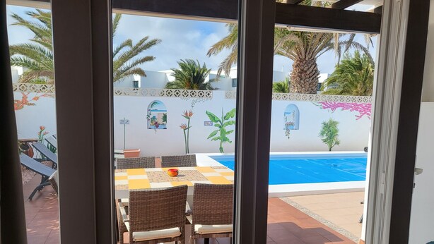 Um pátio externo com mesa e cadeiras, piscina e um muro decorativo com plantas e flores.