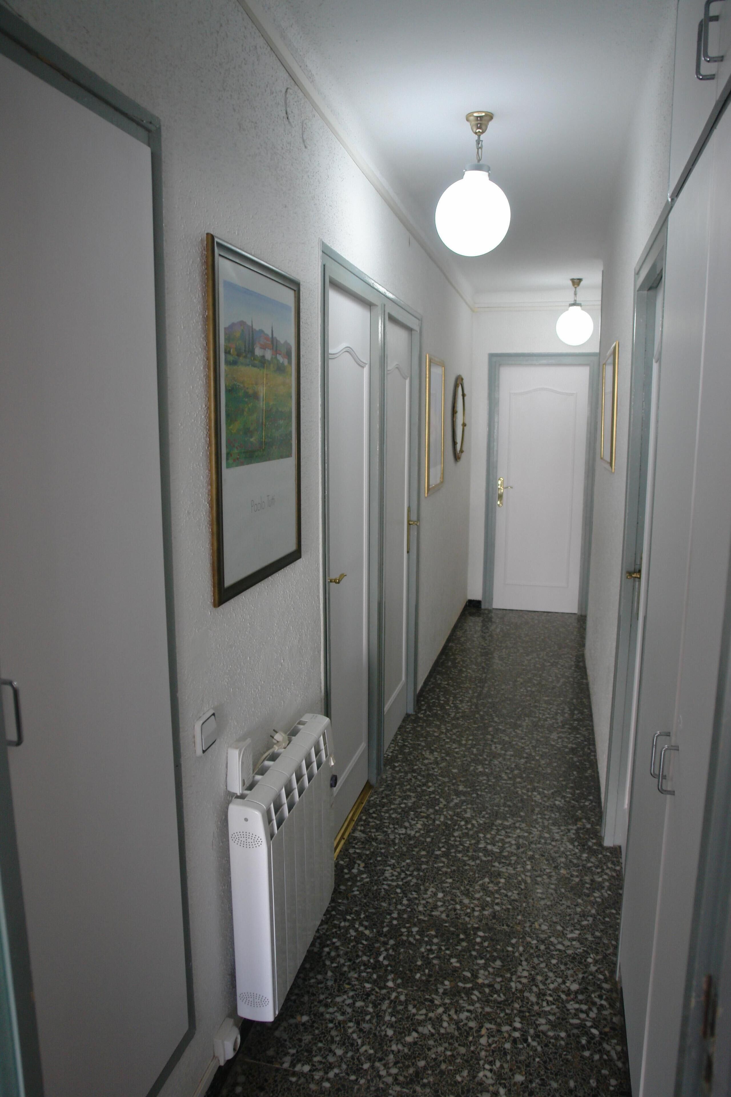 Un couloir étroit avec un radiateur, des œuvres d’art encadrées et une porte au fond.