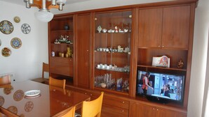A dining area with a wooden table and chairs, a television, and a cabinet with glass doors displaying various items. - Apartment/ flat - Coma-ruga El Vendrell (Coma-Ruga)