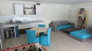 A compact living space with a kitchenette, a dining table with chairs, a sofa, a bookshelf, and a small coffee table.