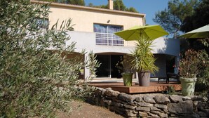 A modern house with a stone wall, a patio with a green umbrella, and potted plants.