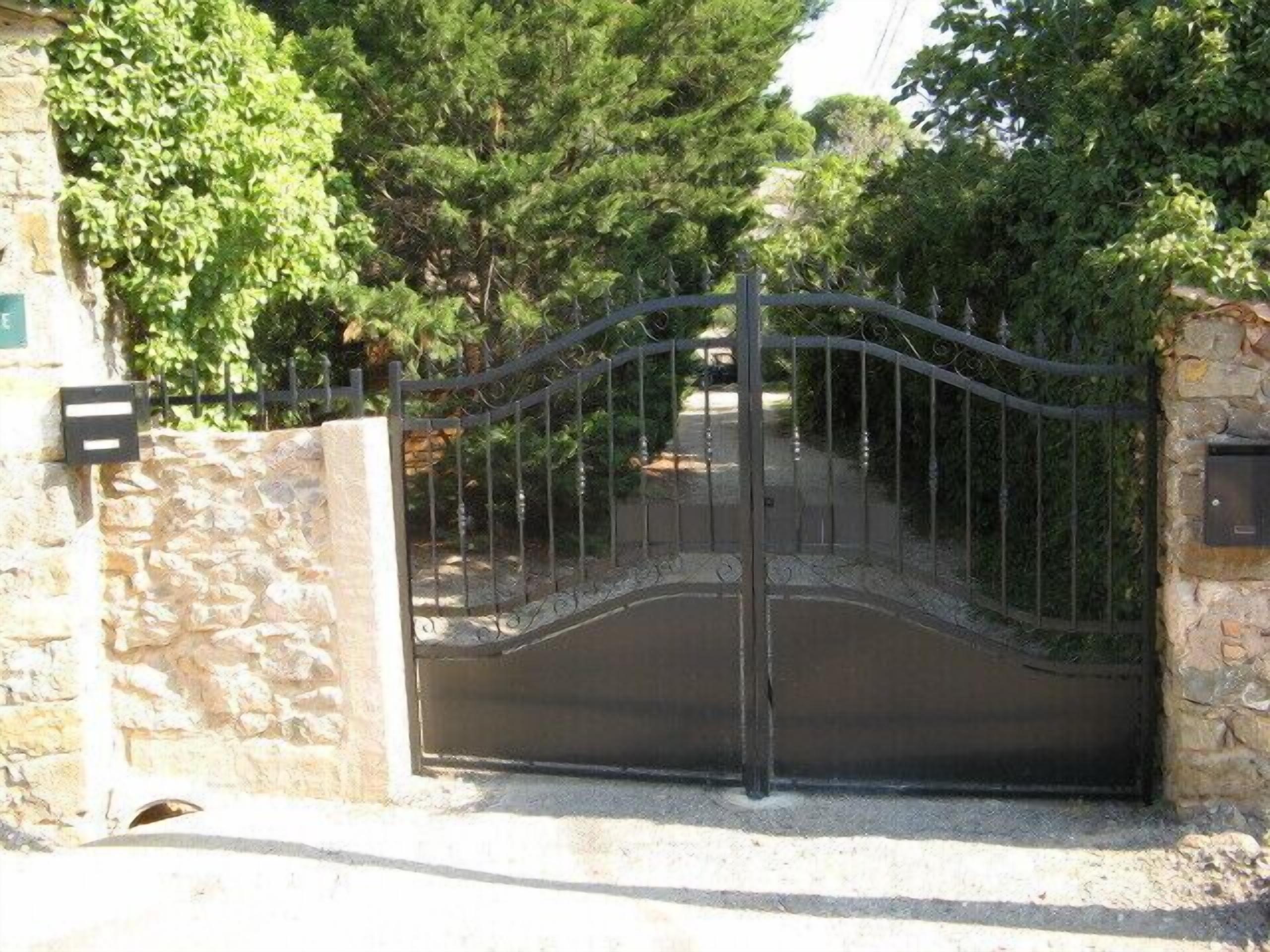 A gated entrance with a stone wall and metal gate, surrounded by trees.
