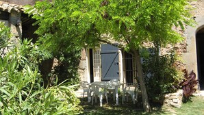 Un edificio de piedra rústico con un porche cubierto que tiene sillas de plástico blanco y una mesa.