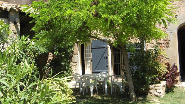 Ein rustikales Steinhaus mit überdachter Terrasse, ausgestattet mit weißen Plastikstühlen und einem Tisch.