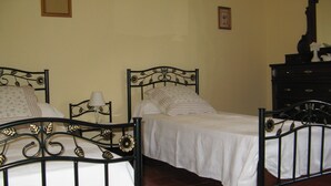 Una habitación con dos camas, cada una con estructura metálica y ropa blanca. Hay un aparador de madera con un espejo y una pequeña foto en el marco en la pared.