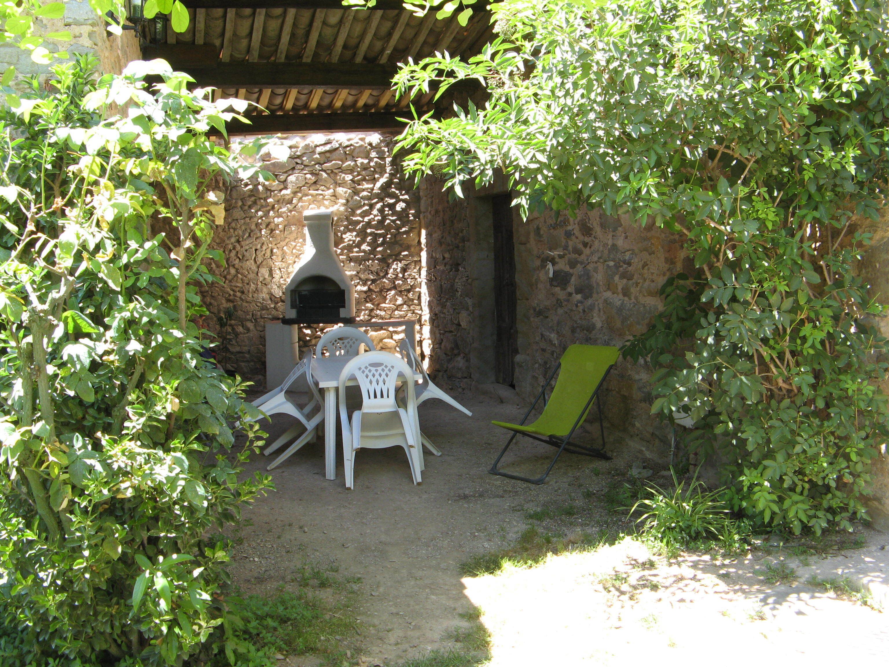 A rustic outdoor seating area with a stone wall, a pizza oven, and a table with chairs.