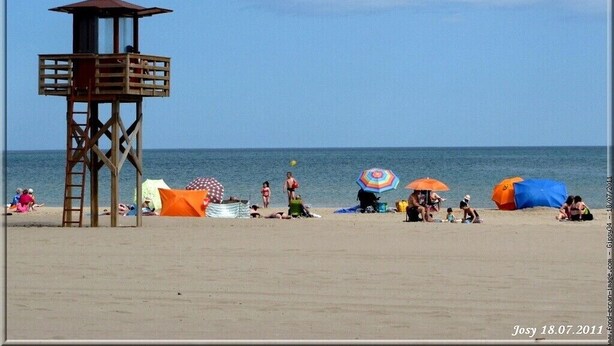 Una playa con una torre de salvavidas, sombrillas y gente relajándose.