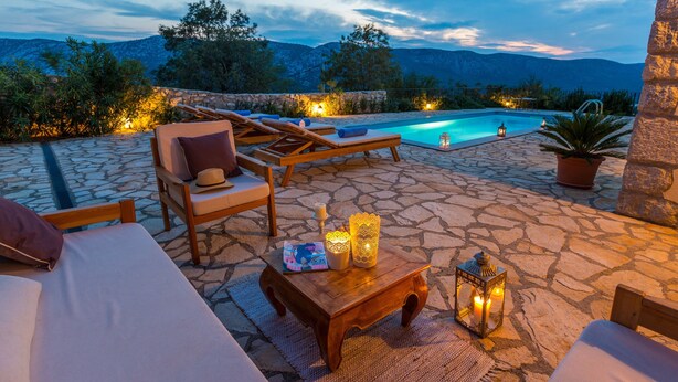 A poolside area with lounge chairs, a wooden table with candles, and a view of mountains.